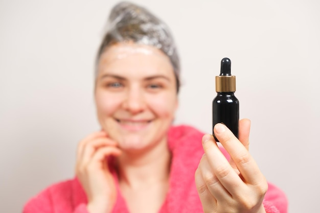 A woman with a film on her head holds a bottle of natural hair oil