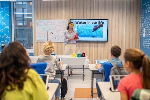 Photo woman with flask looking at kids in class