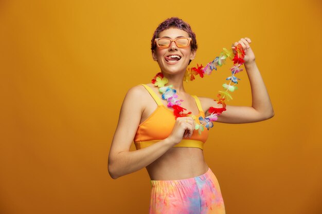 Woman with floral Hawaiian wreath around her neck has fun dancing and smiling in bright clothing against an orange background