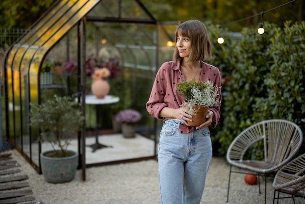 Donna con vaso di fiori in giardino con serra dietro