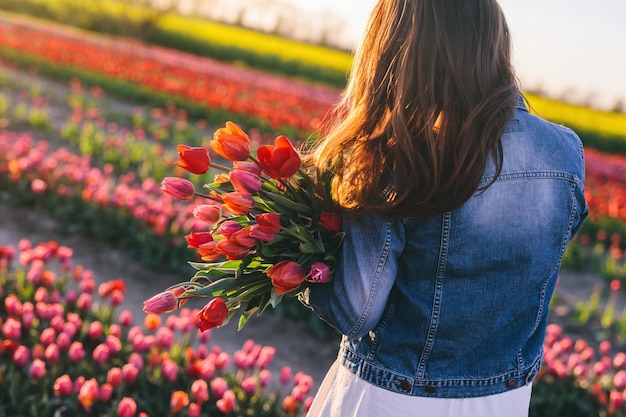 Woman with flowers bouquet on tulip field in spring Sunset light