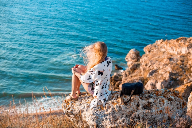 A woman with flowing hair sits on a mountain top and looks out to the sea travel and tourism