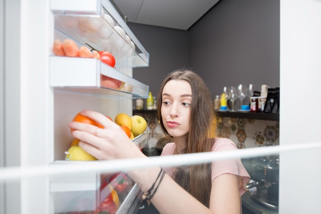 冷蔵庫の近くに食べ物を持つ女性