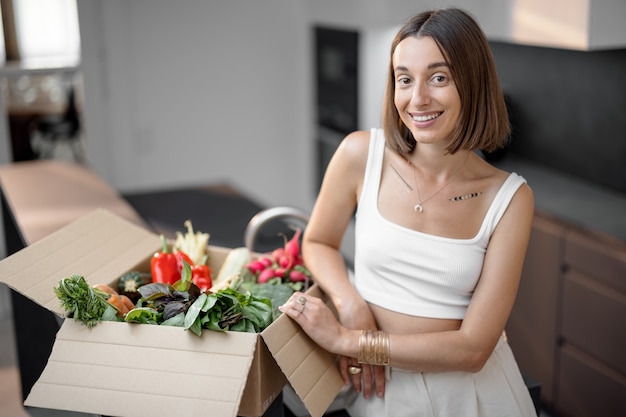 Женщина со свежими овощами, упакованными в картонную коробку на кухне