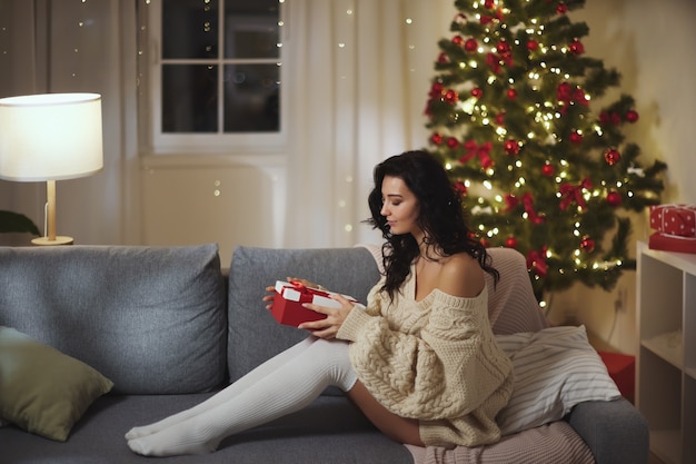 Woman with gift box near christmas tree at home