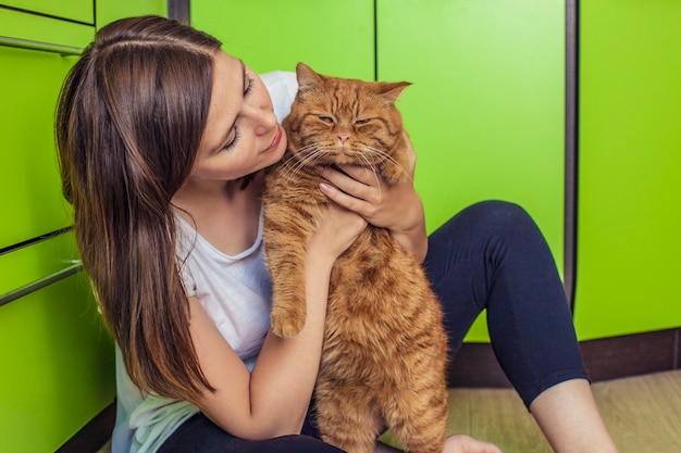 The woman with a ginger cat in her arms cuddling on the bright kitchen