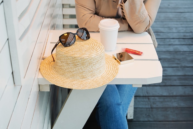 カフェの夏のベランダのテーブルにコーヒーを片手に女性が座っている。