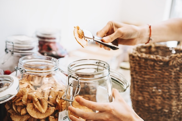 woman with glass jars buying dried berries and fruits in zero waste shop