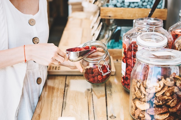 woman with glass jars buying dried berries and fruits in zero waste shop