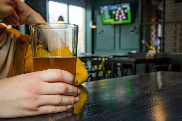 Woman with a glass of light beer watching football match in pub