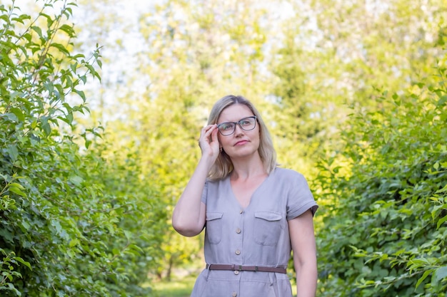 A woman with glasses among the trees holds glasses on face