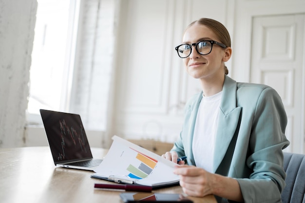 A woman with glasses for a computer freelancer works uses a
laptop makes a report