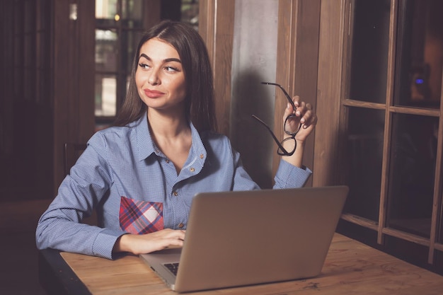 Woman with glasses in her hand is working with grey laptop