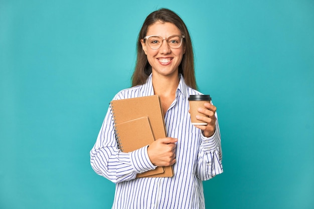 A woman with glasses holding a coffee cup and a book