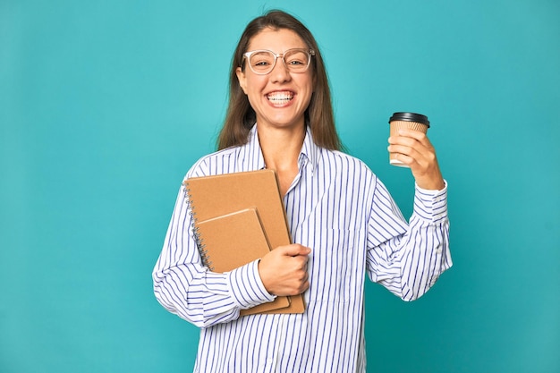 A woman with glasses holding a coffee cup and a book