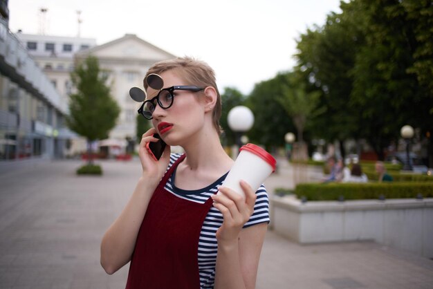 写真 飲み物とグラスで電話で話している通りでメガネをかけた女性