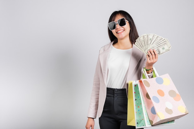 Woman with glasses shopper smile holding online shopping bags and dollar money banknotes on hand