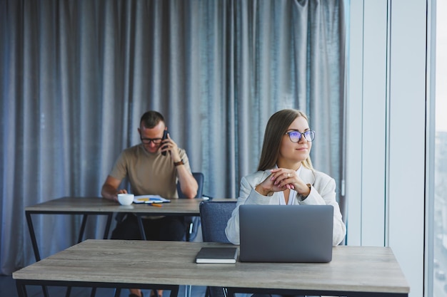 Woman with glasses at the table while working with colleagues in the office Concept of modern successful business people Man and woman sitting at wooden tables