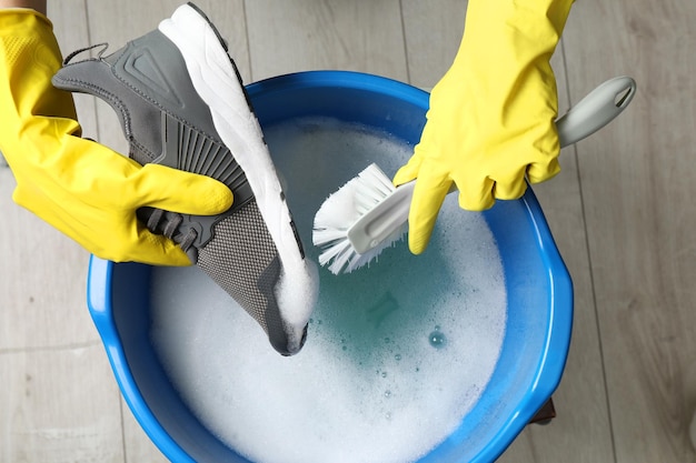 woman with gloves and brush cleaning stylish sneakers in wash basin top view