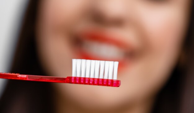 Woman with great teeth holding tooth-brush in front of camera. Blurred background.