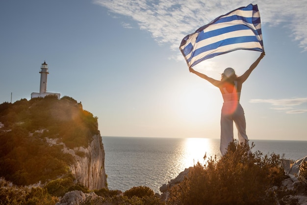 Woman with greece flag looking at sunset above the sea