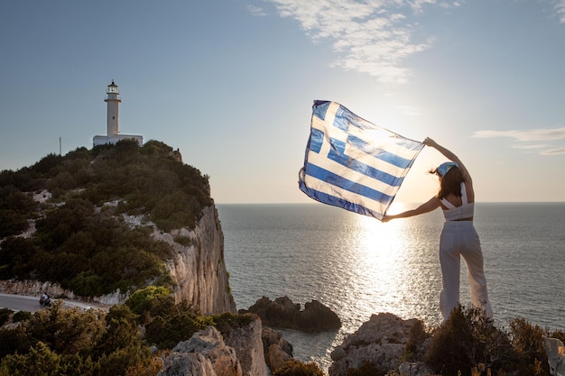 Woman with greece flag looking at sunset above the sea