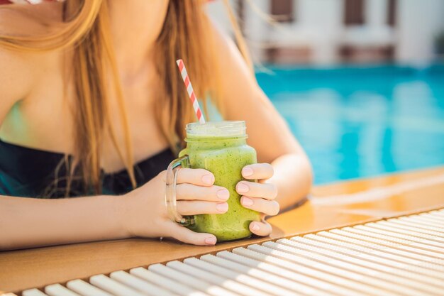 プールの背景にほうれん草とバナナの緑のスムージーを持つ女性健康食品健康的なスムージー