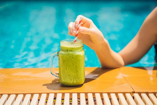 Donna con frullati verdi di spinaci e banana sullo sfondo della piscina frullati sani di cibo sano