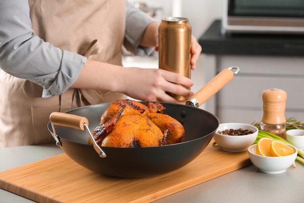 Woman with grilled beer can chicken in pan on cutting board