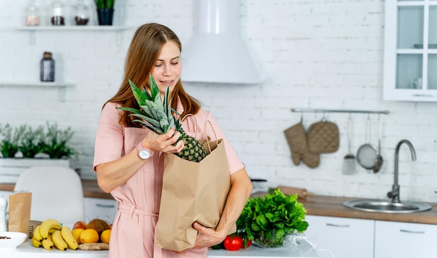 Woman with the grocery store packet in the hands Kitchen background Young woman with healthy food Pineapple in carton packet or bag