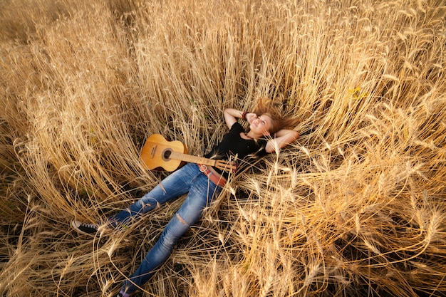 Женщина с гитарой лежит на пшеничном поле