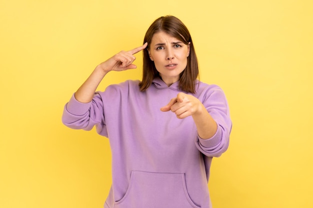 Photo woman with hair holding finger near temple and pointing on you showing stupid gesture