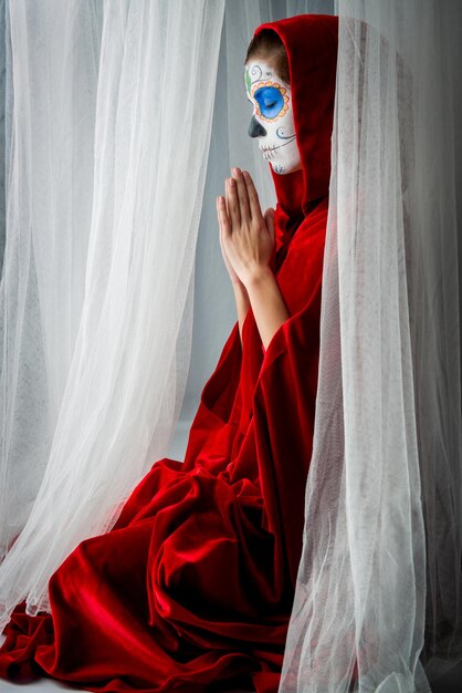 Photo woman with halloween make-up praying while sitting amidst curtains