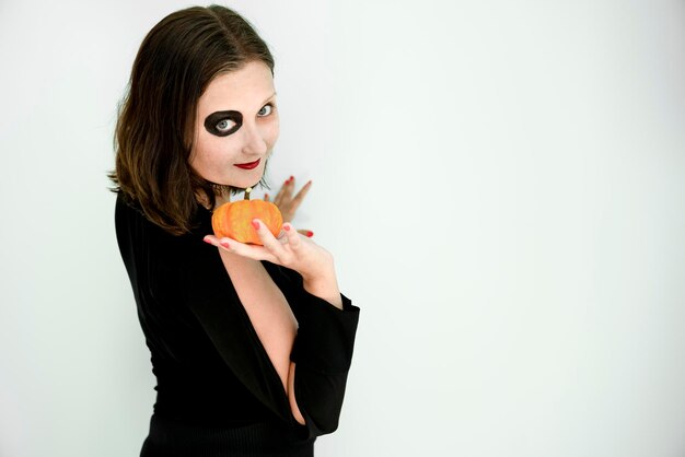 Woman with Halloween makeup on face and pumpkin in hands.