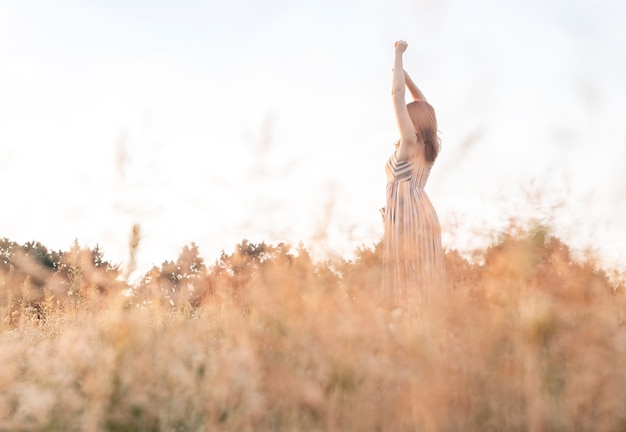 Woman with hands raised up in summer field enjoying freedom and landscape pleasure of being free in ...