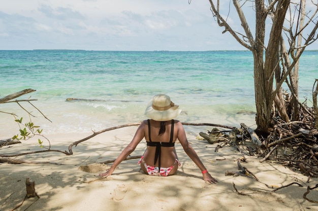 写真 カルタヘナの島のビーチを見て砂の上に座っている帽子とビキニの女性