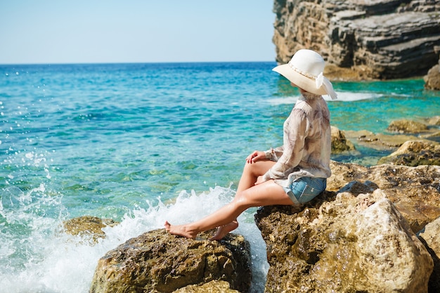 Woman with hat sitting on rocks at the beach