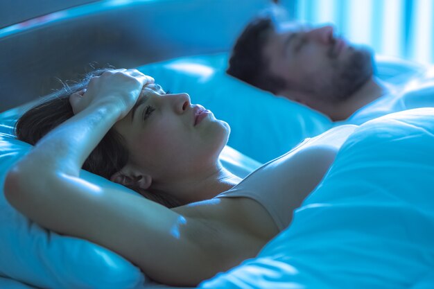 Photo the woman with a headache lay near the man in the bed. night time