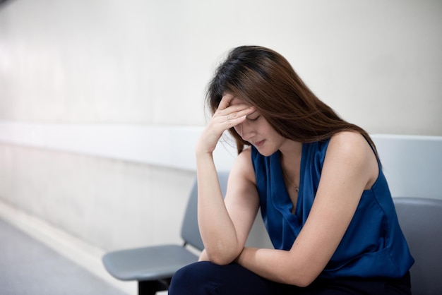 woman with headache sitting on seat against wall