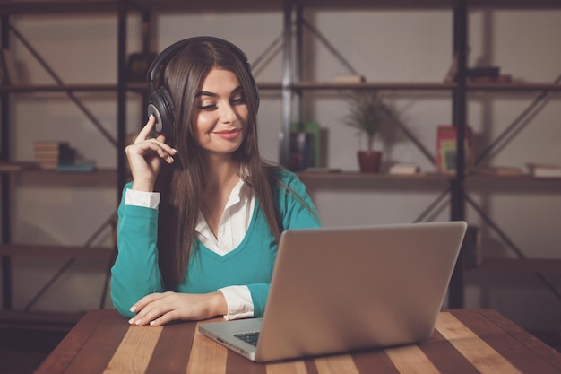 Woman with headphones is sitting at the table with laptop