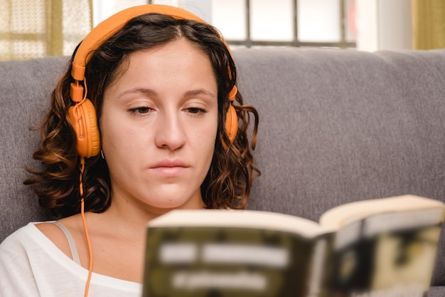 woman with headphones reading a book in the living room sitting on the couch