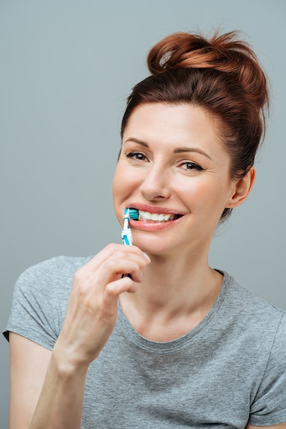 Женщина со здоровыми белыми зубами держит зубную щетку и улыбается концепции гигиены полости рта