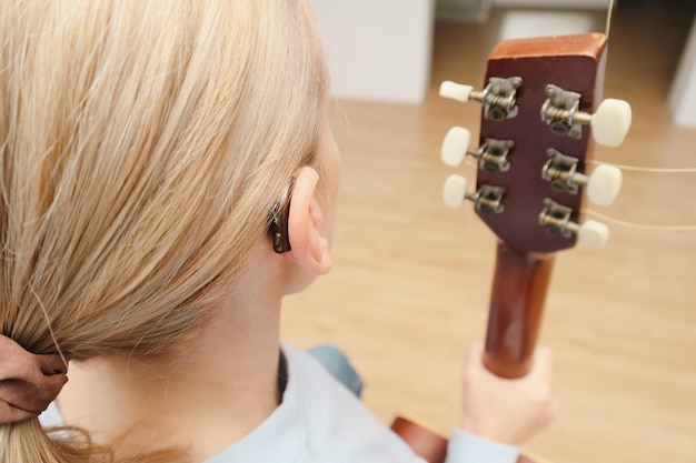 Photo a woman with hearing loss can hear and play guitar again using a hearing aid adult woman with hearing aid behind the ear can hear sounds