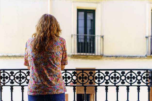 A woman with her back leaning out onto the balcony of her house on a sunny and hot day