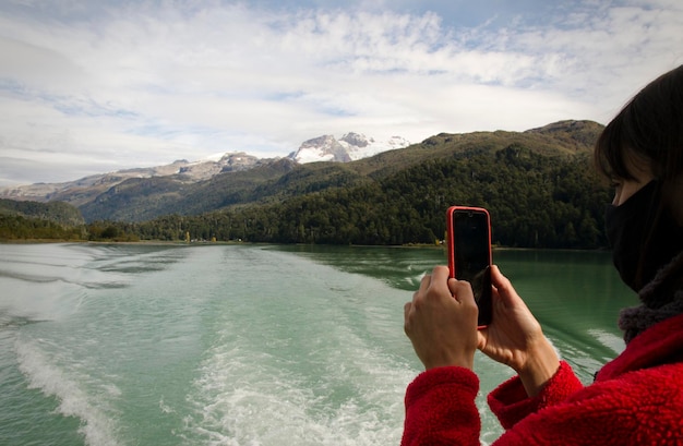 山や湖をボートから写真を撮る携帯電話の女性