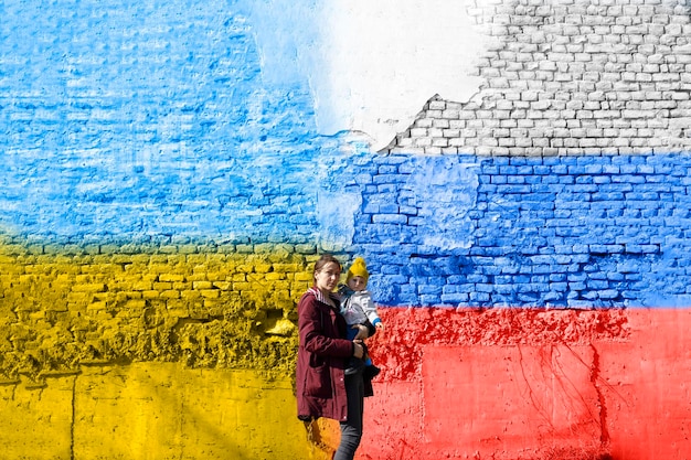 A woman with her child in front a wall painted in Ukrainian and Russian flagtruce concept