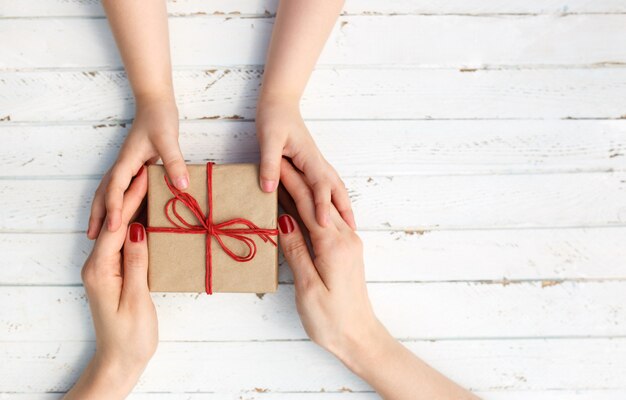 Woman with her child holding a gift in hand on white wooden background.