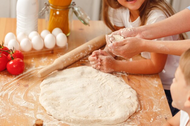 Женщина с детьми замешивает тесто на кухне