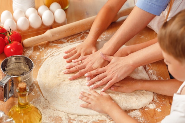 Woman with her children kneading dough in kitchen