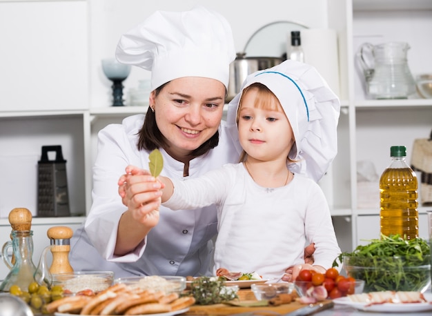 La donna con sua figlia sta cucinando l'insalata in uniforme nella cucina